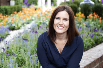 Erin Troups looks into the camera for a photo outside in front of a flower garden.