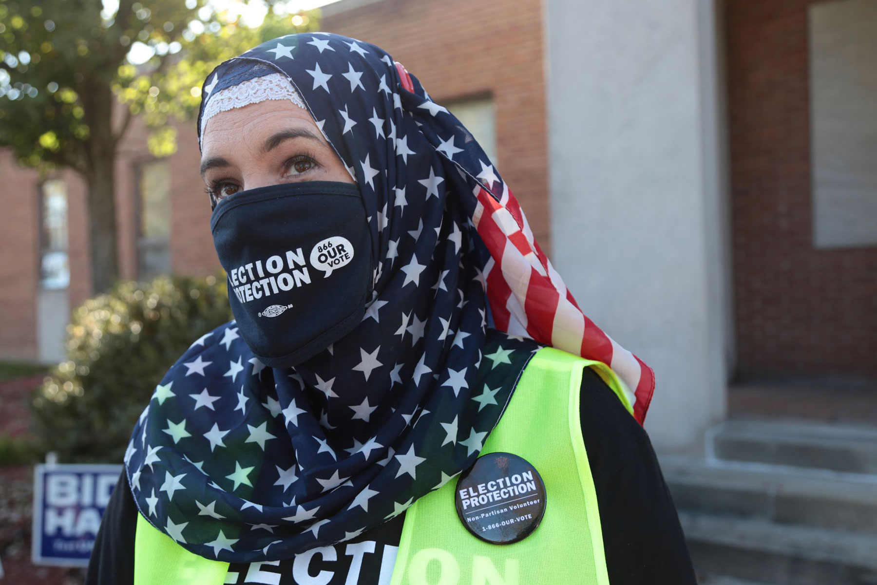 A person in a hijab with an American flag print and a face mask that says election protection.