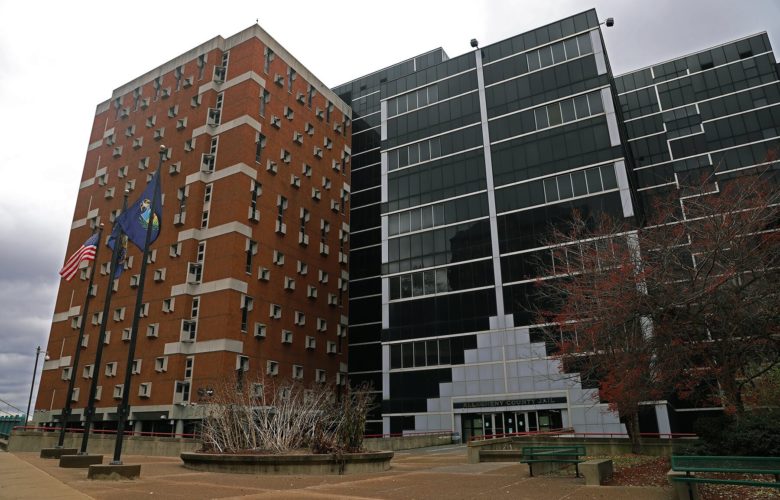 The front facade of Allegheny County Jail. The building is constructed of long, rectangular glass panels in the center and red brick on the left side.