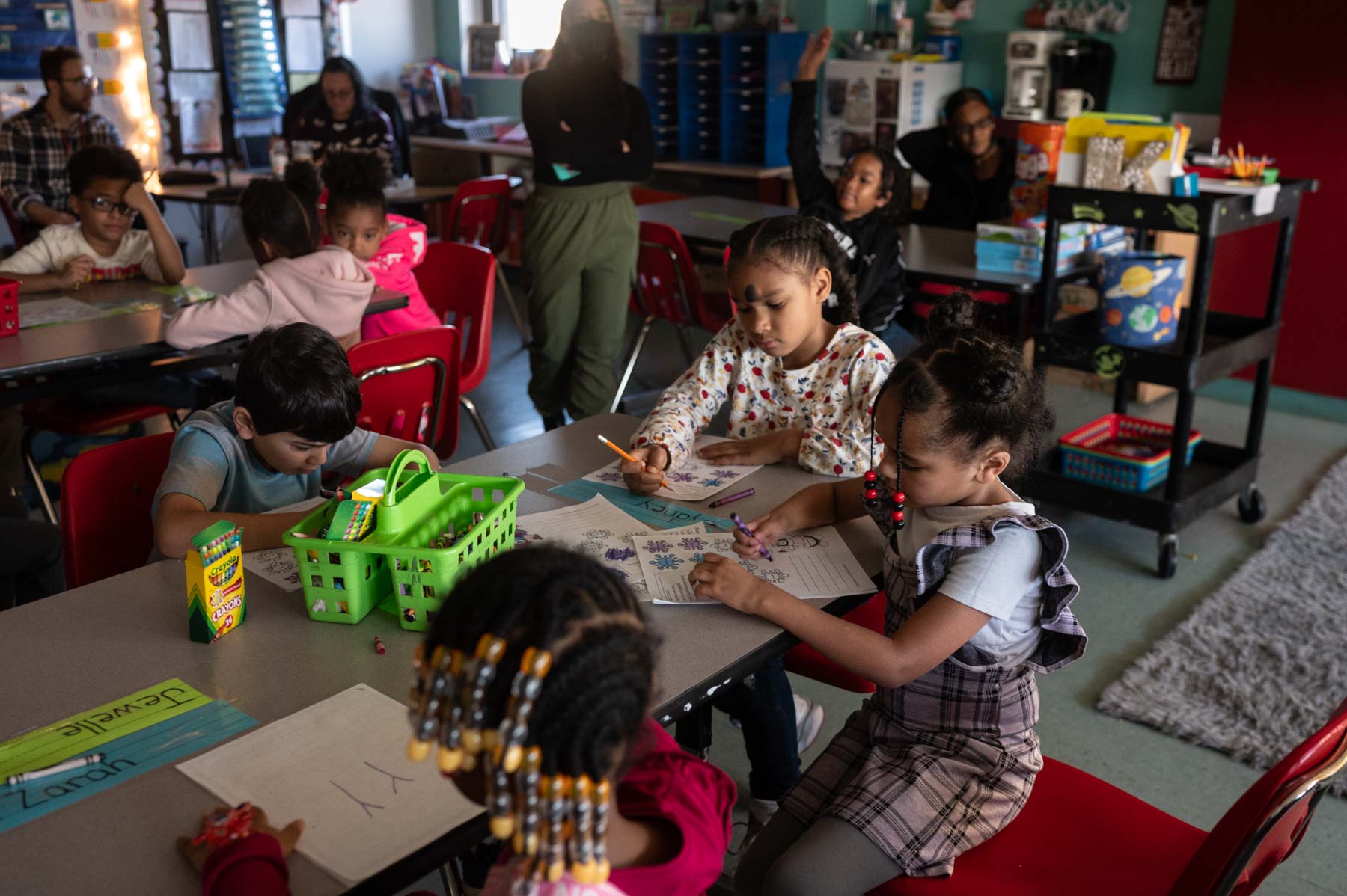 children draw with crayons while sat around a table in a classroom.