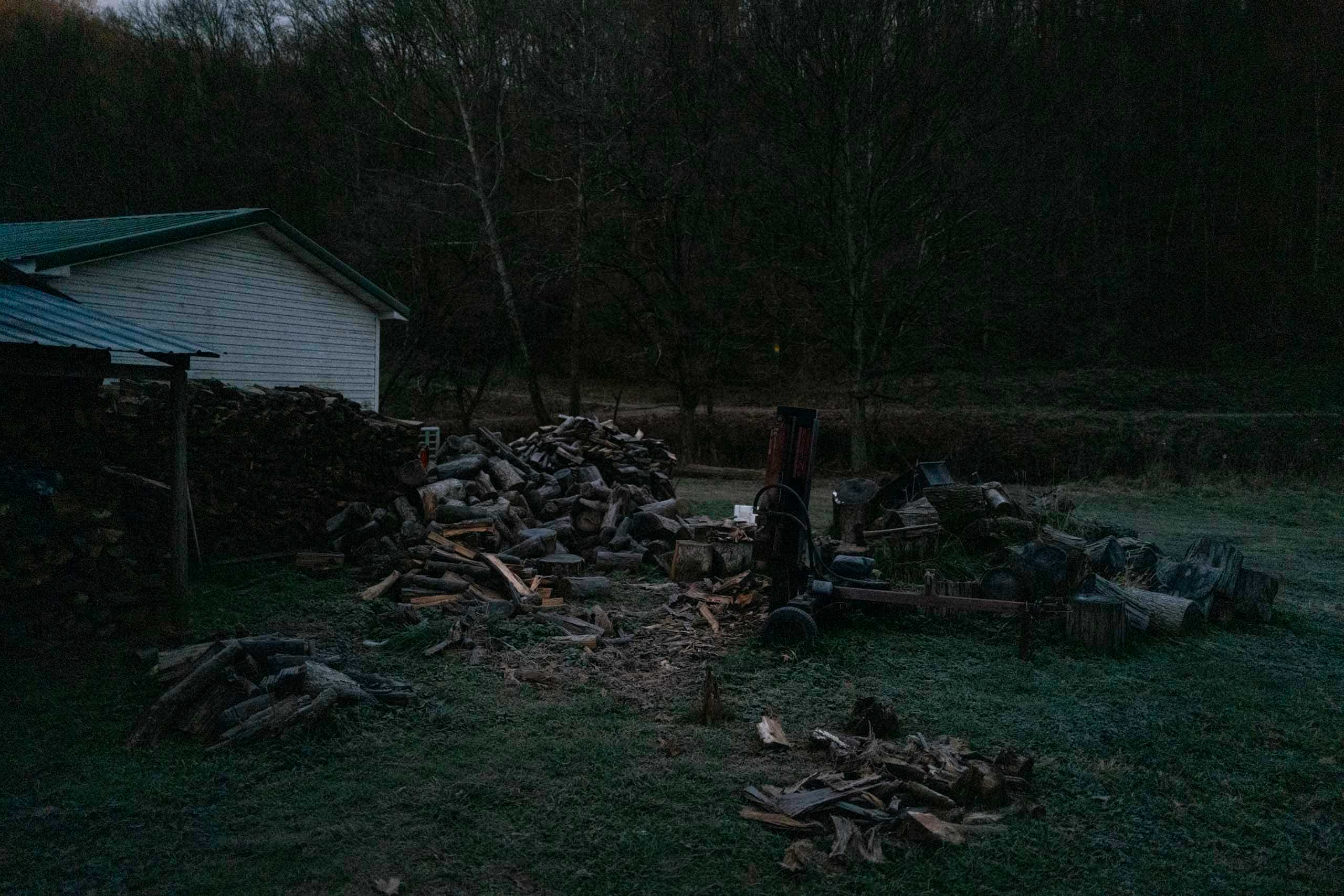A pile of wood in front of a house at dawn.