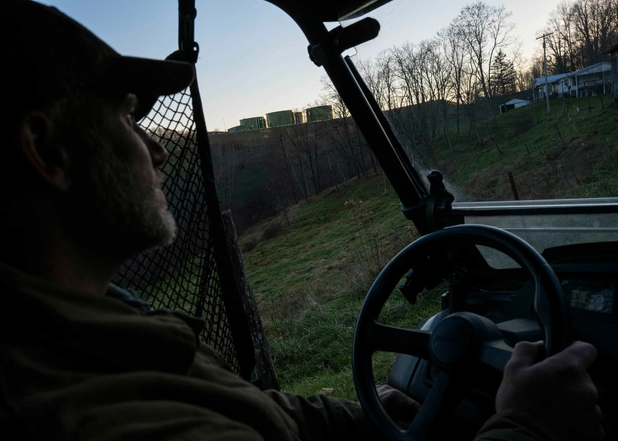 A man drives an ATV up a hill towards four large wastewater tanks.