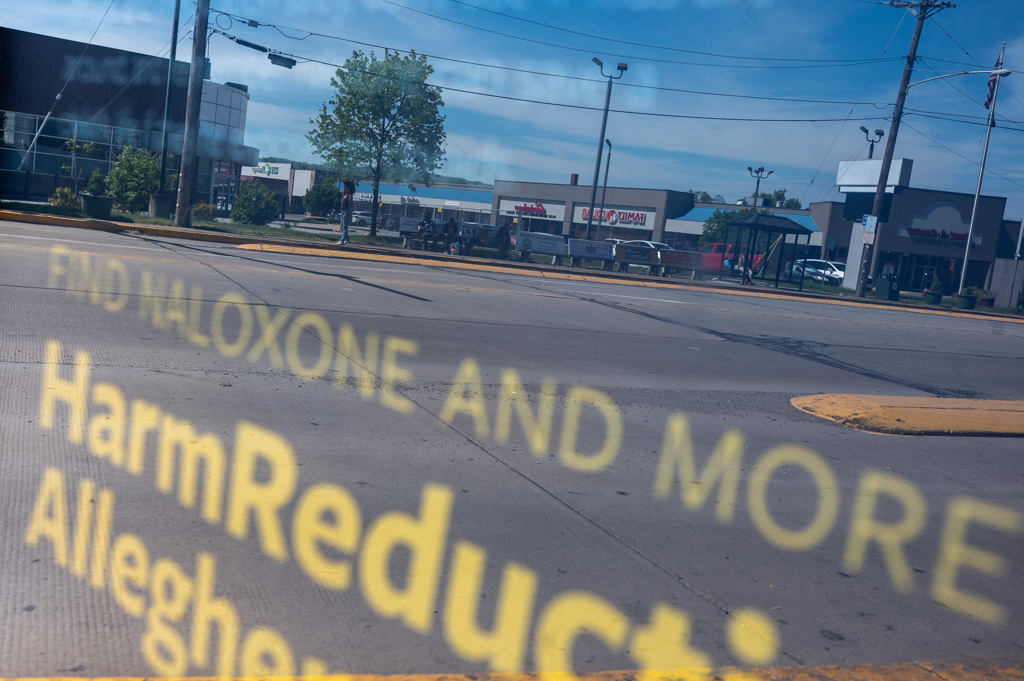 A street scene with buildings and shops is visible through a glass window. The text 