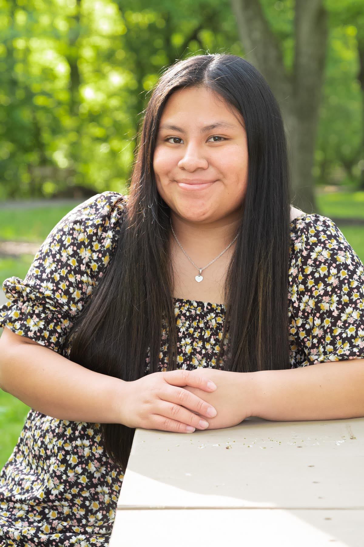 Natalia Connor sits at a picnic table outdoors in a park, smiling at the camera, representing the importance of amplifying youth voices in decision-making.