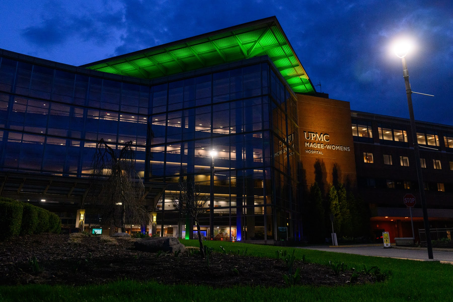 UPMC Magee-Womens Hospital building at night, with lights on inside and green illumination on the roof.