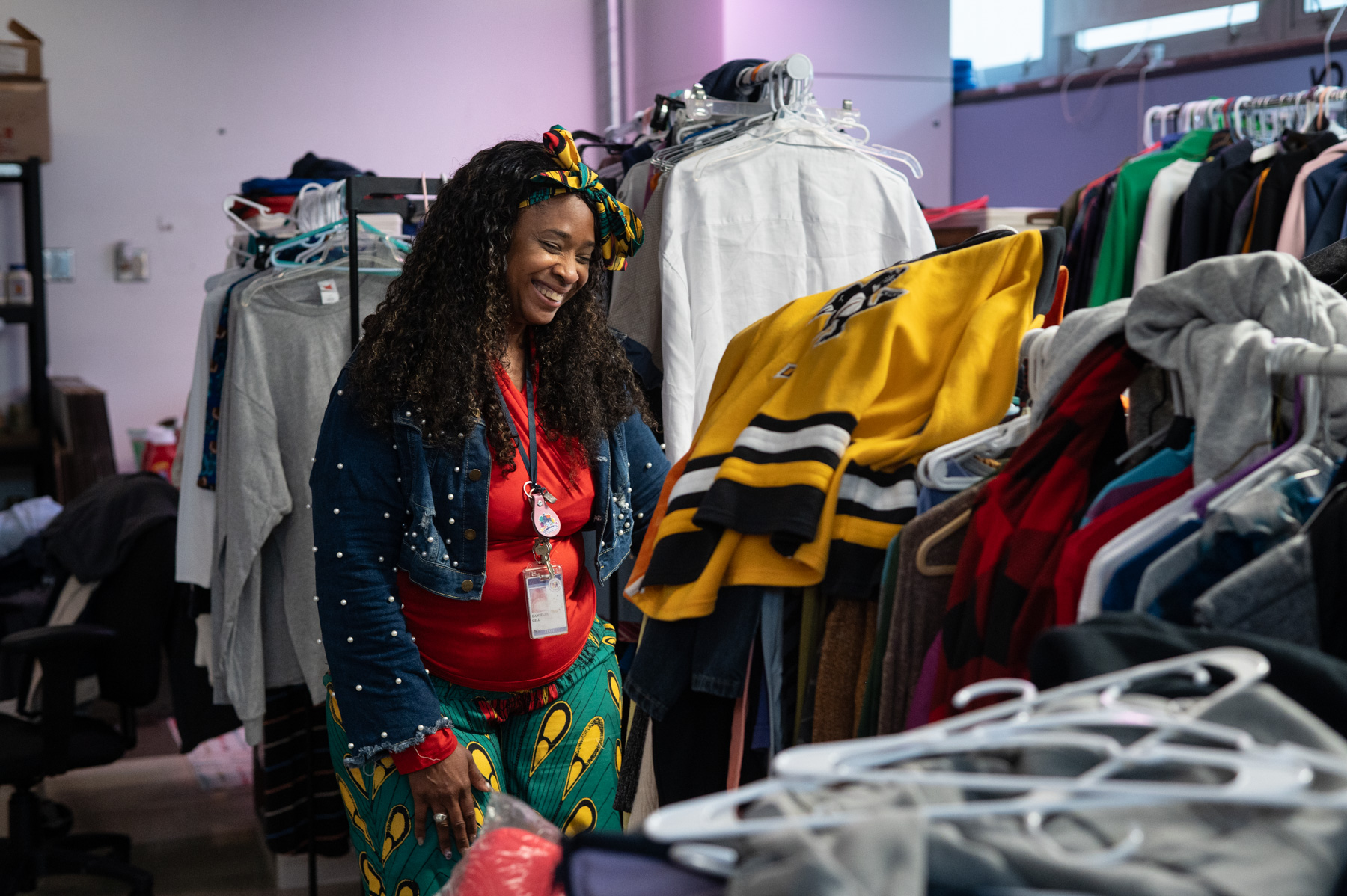 A woman browses through racks of clothing in a store or donation center, smiling while looking at garments.
