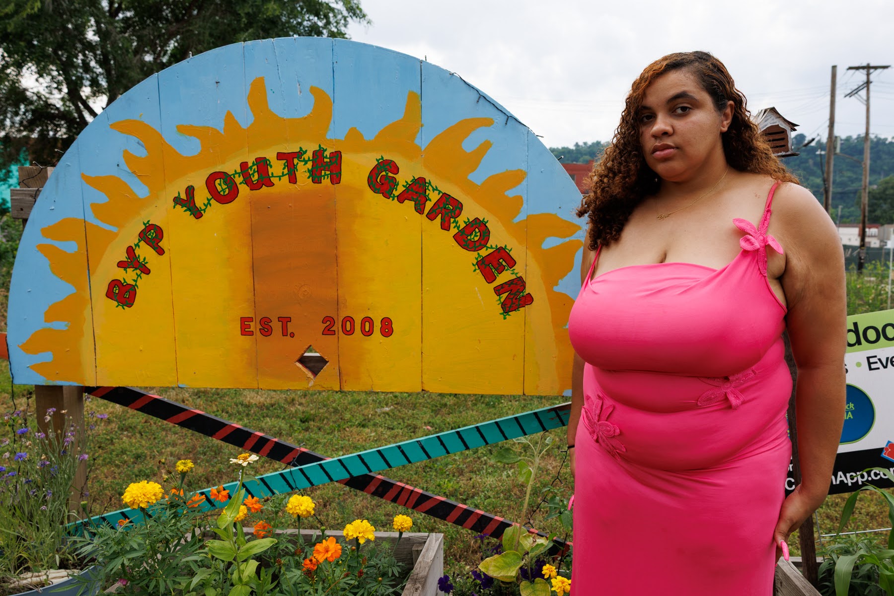 A woman in a pink dress stands in front of a colorful sign that reads