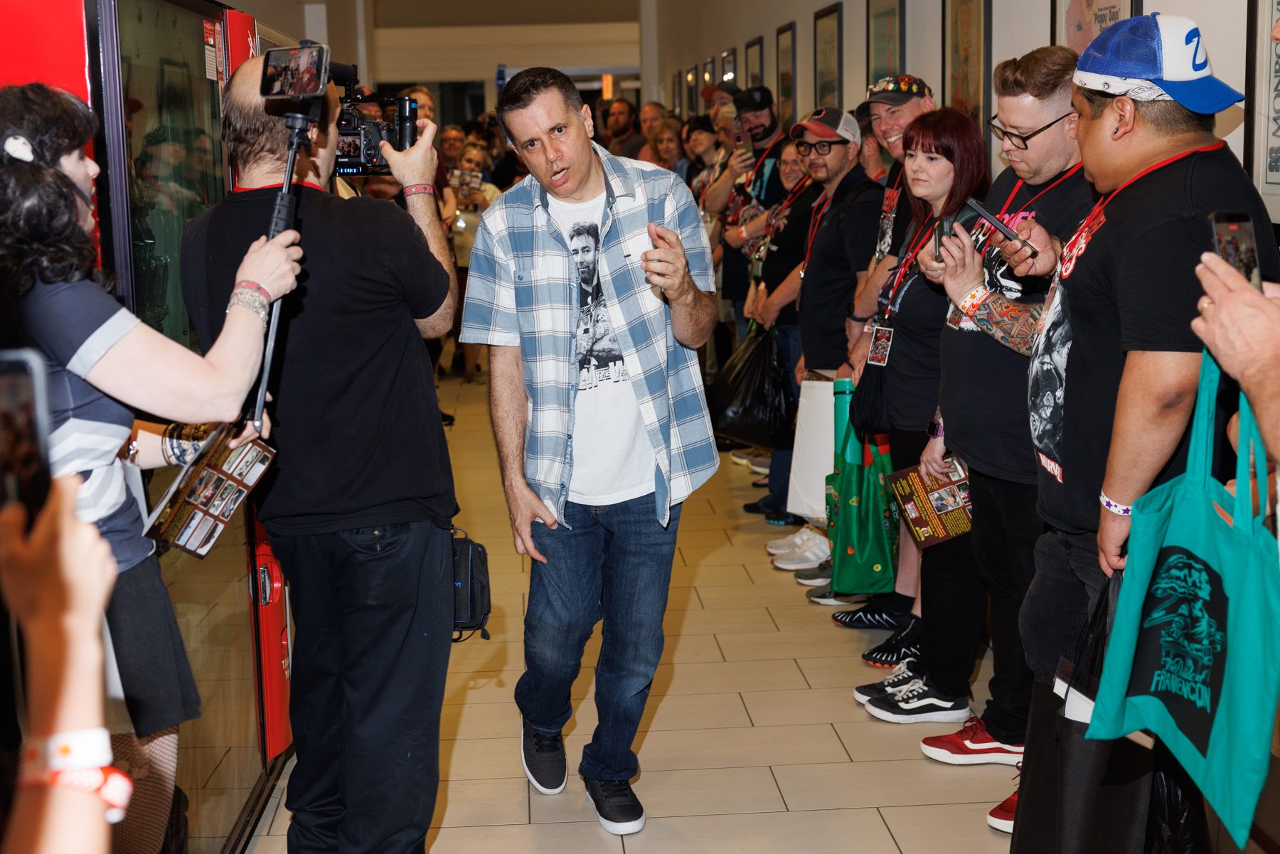 A man walks down a hallway lined with people on both sides, some recording with phones and cameras.