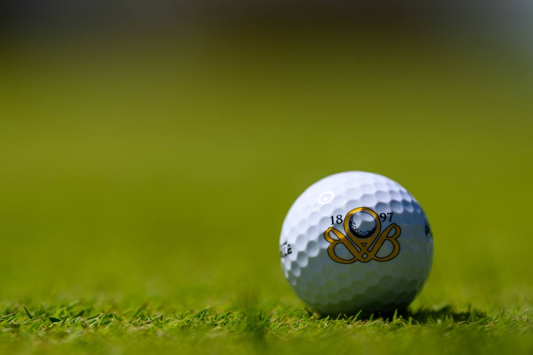 A close-up of a golf ball with a logo and the year 1897 printed on it, resting on a green grass surface.