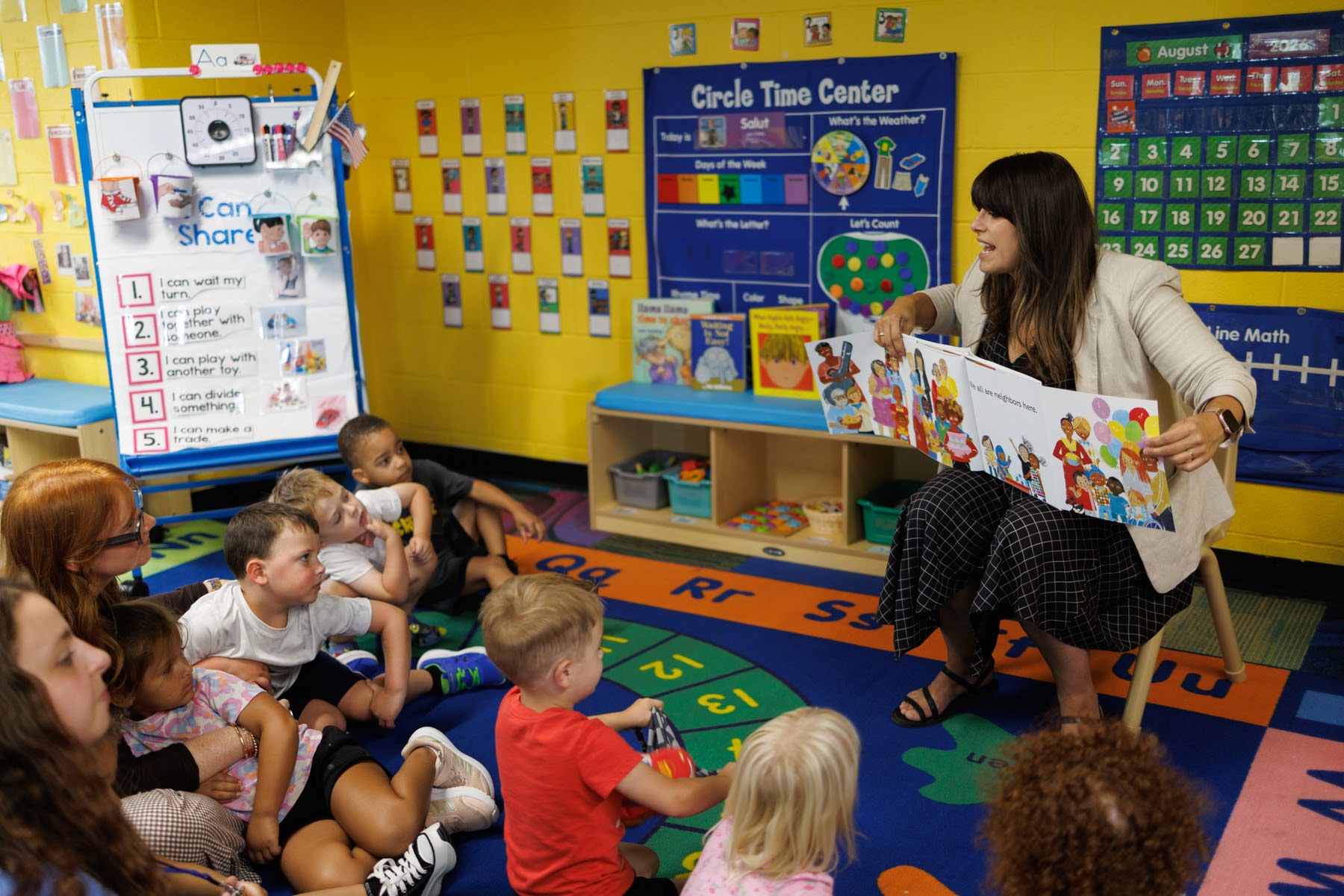 Allegheny County Executive Sara Innamorato reads a picture book to a group of young children seated on the floor in a colorful classroom.