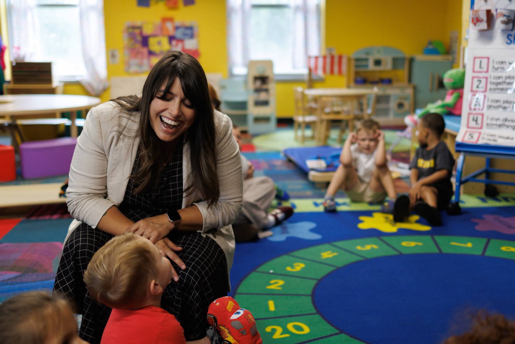 County Executive Sara Innamorato smiles and talks with a young child in a colorful classroom while other children sit and interact in the background.