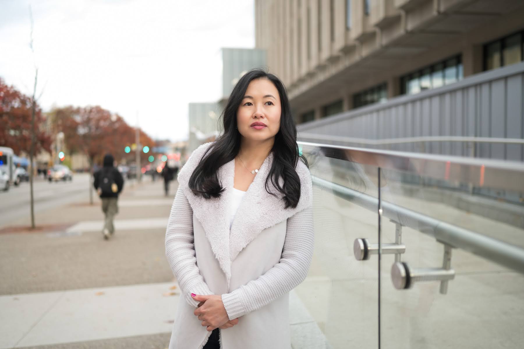 A woman standing on a city sidewalk next to a glass railing.