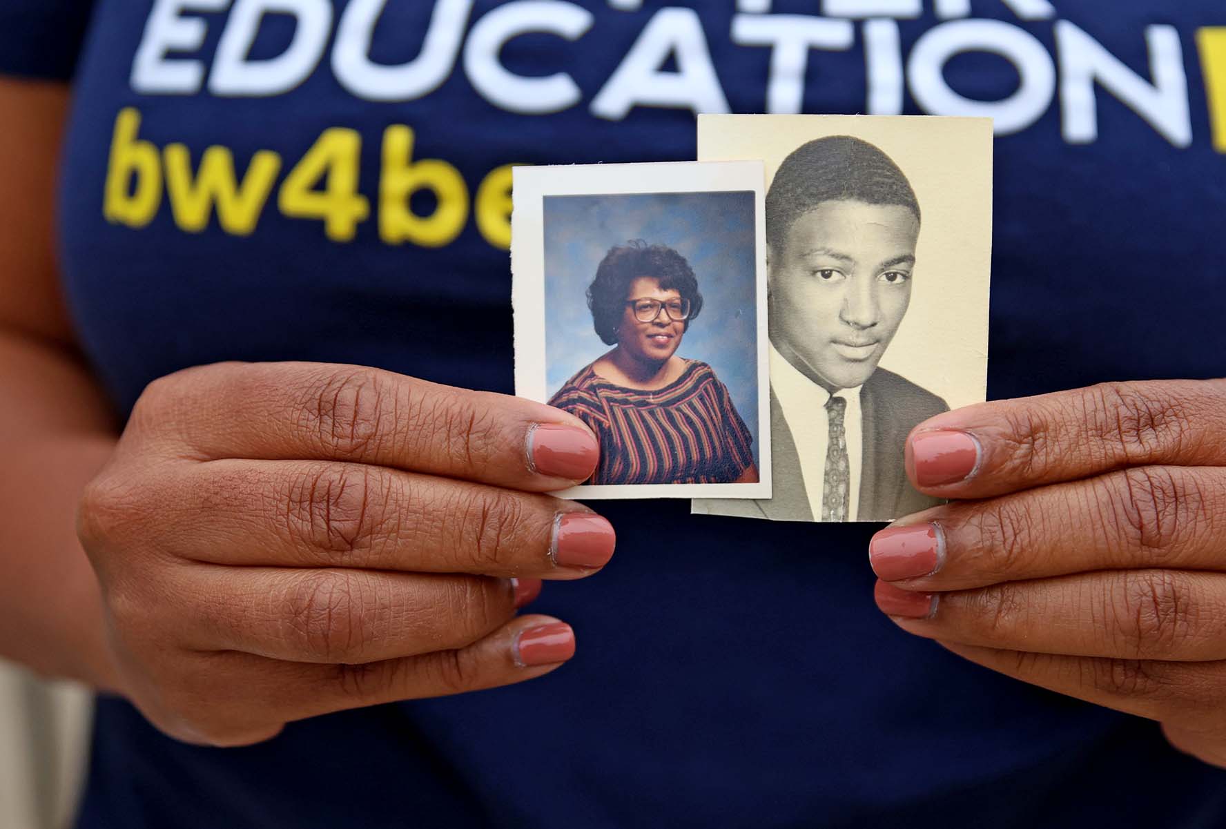A person holding two vintage photographs of an older woman and a young man.